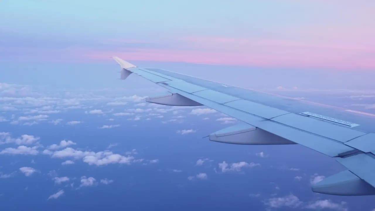 Aircraft wing above scattered clouds under a pink and pale-blue sunset sky